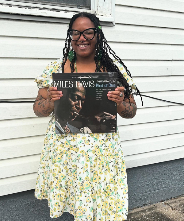 Ashley smiling while holding a Miles Davis “Kind of Blue” vinyl record outdoors