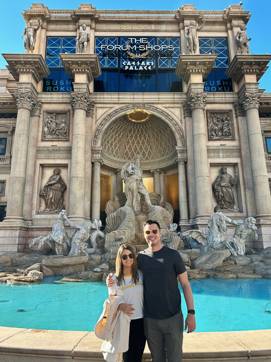Renan smiling with a companion in front of a fountain at The Forum Shops at Caesars Palace in Las Vegas
