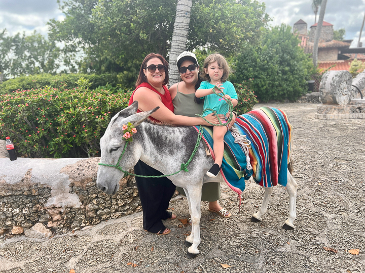 Analys and family smiling outdoors while her niece sits on a donkey during a sunny day