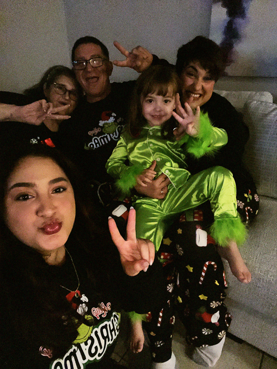 Analys posing with family in festive pajamas, smiling and making peace signs on a couch
