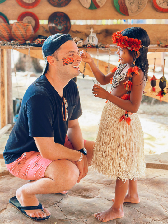 Renan smiling as a child paints traditional designs on his face during a cultural experience